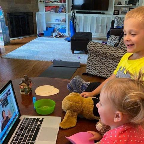 Two young children with stuffed animals looking a story time on a laptop computer