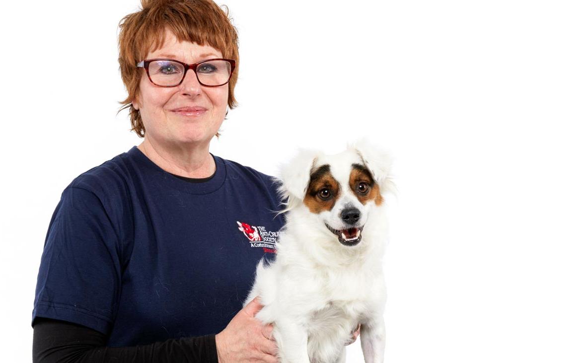 Woman in blue shirt wearing red glasses with red hair holding white dog with brown spots on his eyes