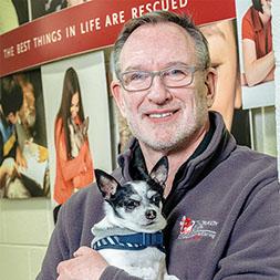 Man in grey fleece sweater holding small black and white dog