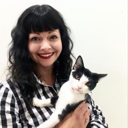 Woman with black hair in a black and white checkered shirt holding a black and white cat