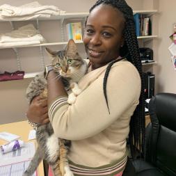 African American woman in tan sweater and pink shirt holding a brown and gray tabby cat