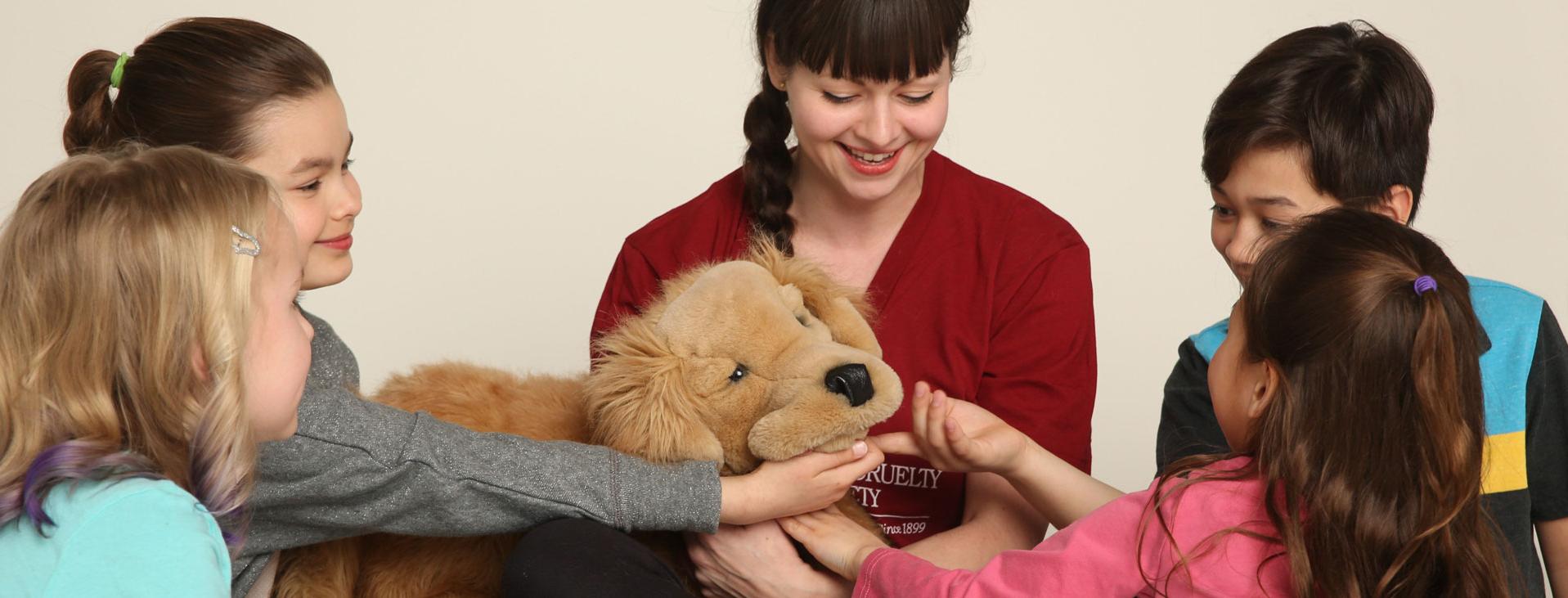 woman with brown hair in a braid holds dog puppet while four children pet dog puppet