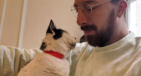 A man with glasses looks at his white foster cat